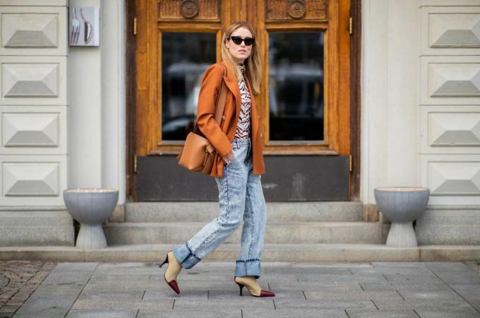 Жінка вуличного стилю в прямих джинсах і помаранчевій курткі