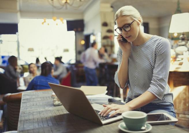 Wanita yang bekerja di laptop dan berbicara di telepon saat berada di kedai kopi