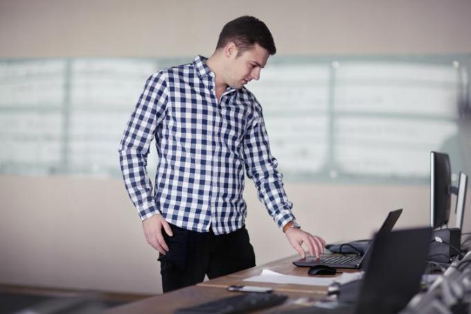 Hombre de pie en el escritorio de la oficina con computadora portátil