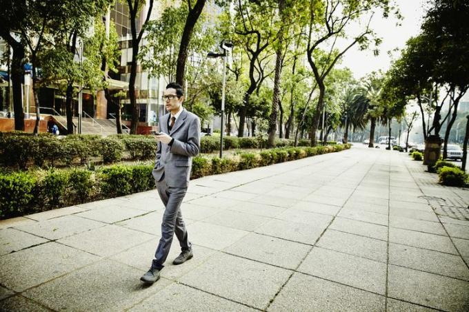 Бизнесмен на тротуаре смотрит на смартфон