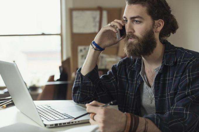 jonge man voor laptop die serieus telefoneert