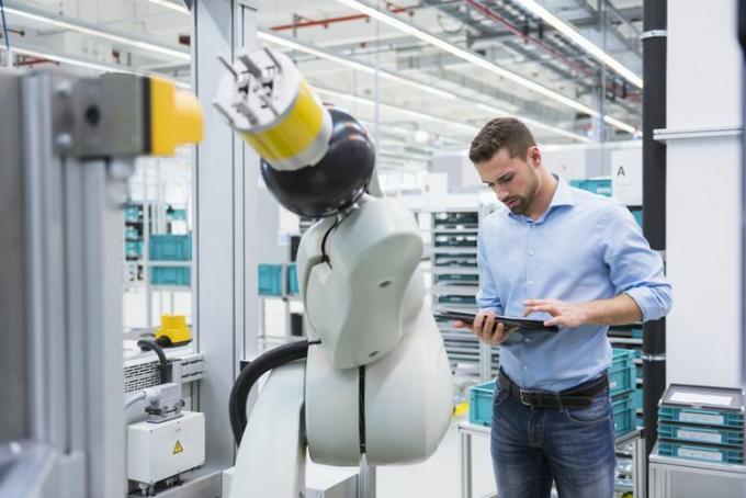 Muž pomocí tabletu nextb k montážnímu robotu v továrně