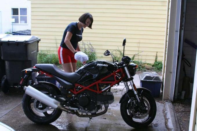 Wanita membersihkan sepeda motor dengan spons besar.