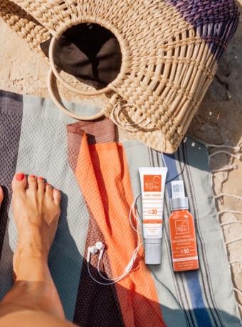 En modellfot på en strand med Suntegrity giftfria självbrunarprodukter liggandes på handduken.
