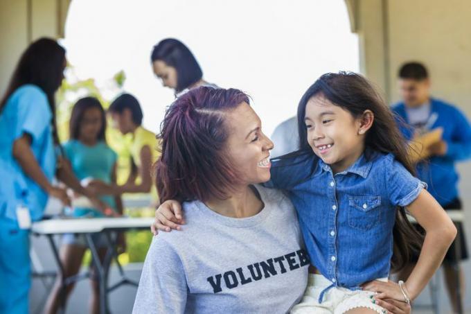 Vrouw in een vrijwilligerst-shirt met een glimlach van een klein meisje tijdens een evenement.
