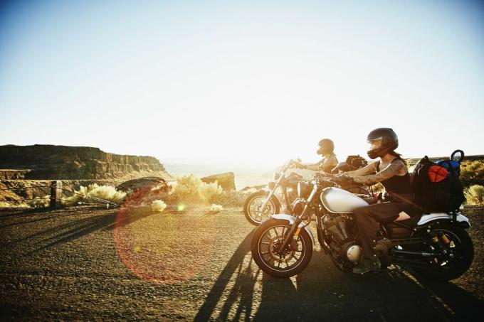 Sievietes motociklistes vasaras vakarā brauc pa tuksneša kanjona ceļu