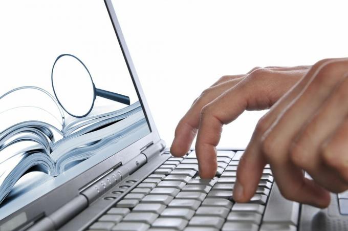 Haku Internetistä, miehen kädet kannettavan tietokoneen näppäimistö, suurennuslasi näytöllä
