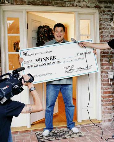Hombre recibe un cheque de mil millones de dólares, entrevistado por un equipo de televisión