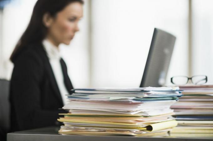 Une employée de bureau avec une pile de dossiers avec de la paperasse sur son bureau.