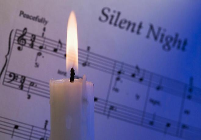 Eine brennende Kerze vor den Noten von " Stille Nacht".