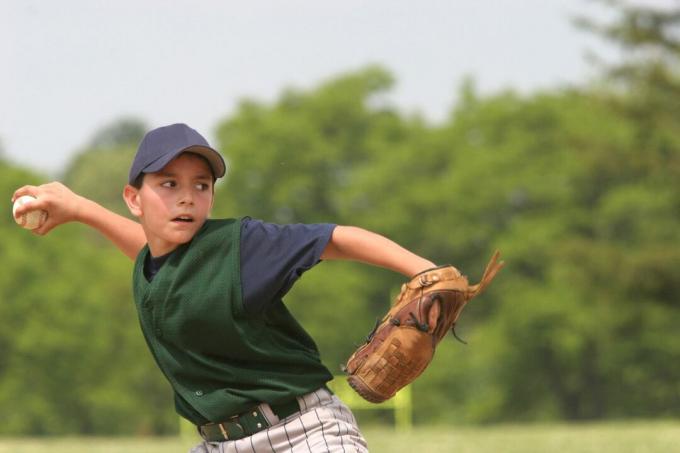 Közepes közelről egy ifjúsági baseball dobó a pályán. Zöld és kék egyenruha.
