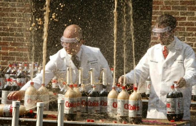 जब आप डाइट कोक में मेंटोस कैंडी डालते हैं तो क्या होता है, इसका प्रदर्शन करते हुए दो वैज्ञानिक।