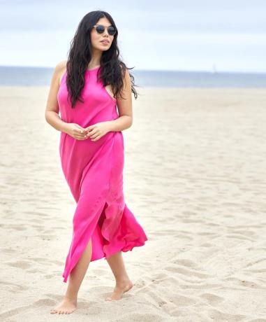 En model i en hot pink underkjole og solbriller går langs stranden.