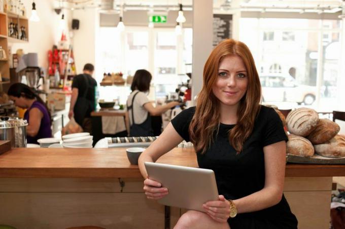 Mujer joven sentada en el mostrador de la cafetería y leyendo su carta de oferta por correo electrónico.