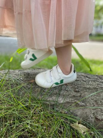 תקריב של רגלי ילד על עץ לבוש נעלי ספורט של Veja.