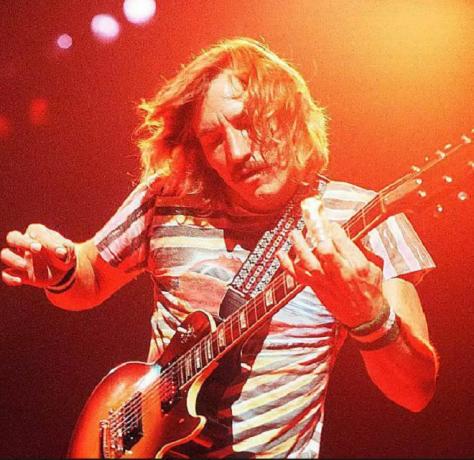 Joe Walsh de la Eagles cântă live pe scenă cu chitara.