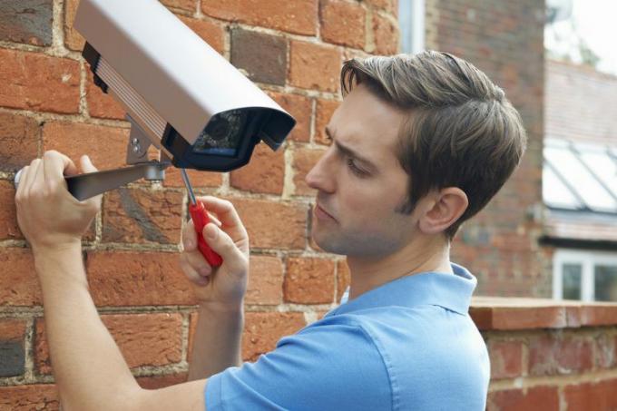 Un técnico colocando una cámara de seguridad en la pared de una casa