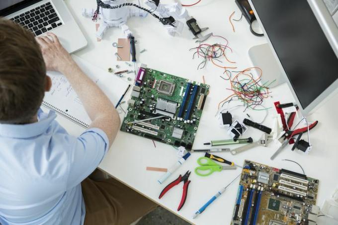 Un om de reparații de computere care lucrează la un laptop înconjurat de o placă de bază și unelte