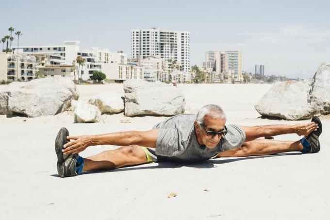 Възрастен мъж прави шпагат на плаж