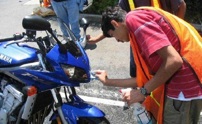 Anak muda membersihkan lampu depan sepeda motor biru.