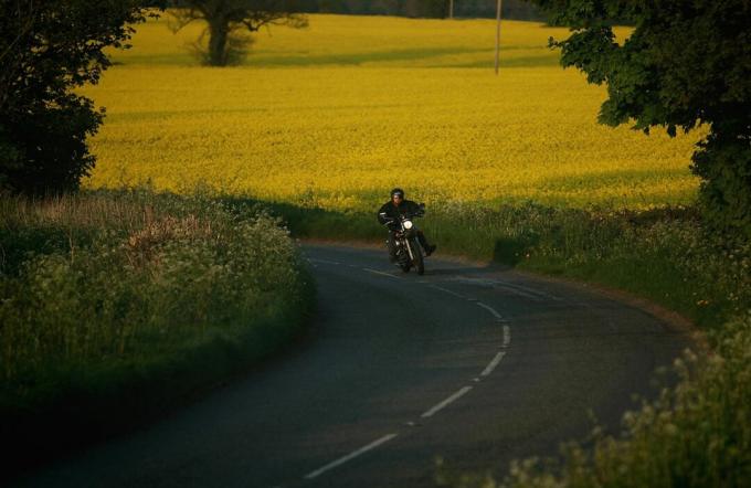 Motociclista que viene alrededor de una curva con campo dorado en segundo plano.