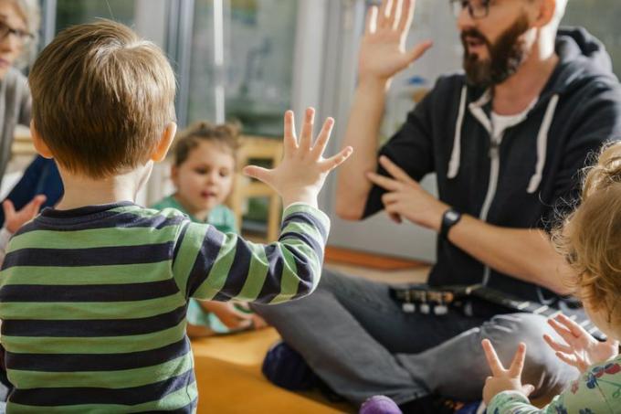 बच्चा हाथ उठाकर दूसरों के साथ गा रहा है और किंडरगार्टन में शिक्षक