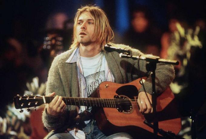 Kurt Cobain sahnede şarkı söylüyor ve gitar çalıyor.