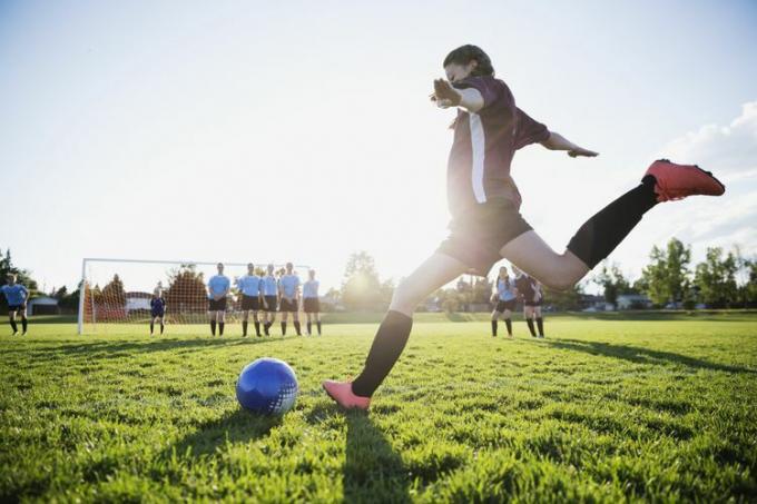 Middle school pige fodboldspiller sparker frispark på solrig mark