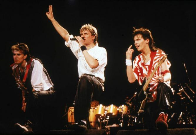 Басистът Джон Тейлър (вляво), певецът Саймън Льо Бон и китаристът Анди Тейлър от британската поп група Duran Duran изпълняват на сцената по време на концерт, 1984 г.