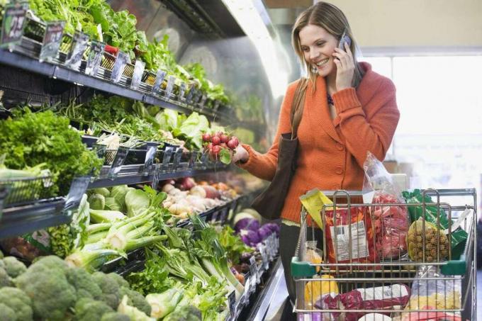 Wanita berbicara di ponsel dengan sayuran di supermarket
