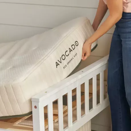 Um close-up de um colchão duplo sendo colocado em uma estrutura de cama com o nome Avocado visível na lateral. 