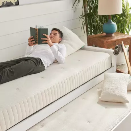 Eine Person liegt auf einer nackten Avocado-Matratze und liest ein Buch. 