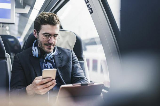 Biznesmen w pociągu z telefonem komórkowym, słuchawkami i tabletem