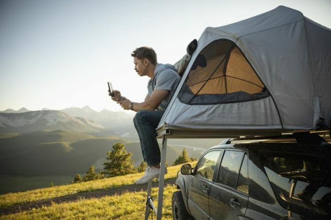 Serene man kamperen, ontspannen bij een SUV-daktent in een zonnig, idyllisch veld, Alberta, Canada