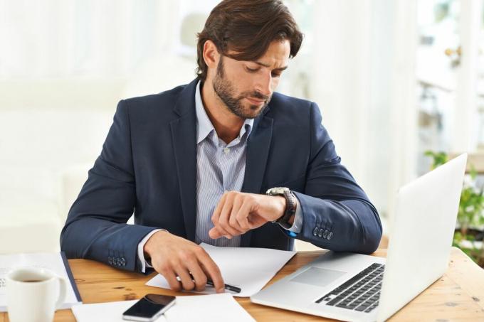 Pria yang bekerja di depan komputer memeriksa jam tangannya