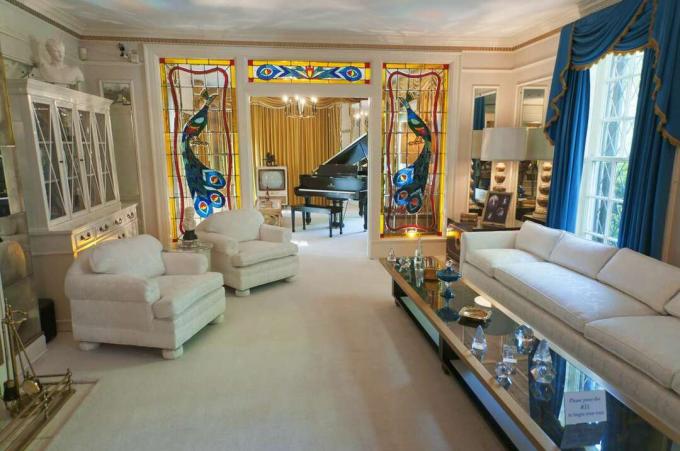 Beyaz mobilyalar ve oturma odasının halıları boyalı camdan müzik odası ve kuyruklu piyanoya bakıyor
