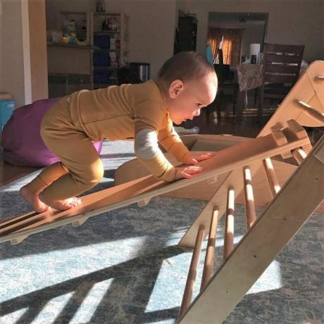 Un bébé grimpe sur une rampe jusqu'à un triangle de Pikler.