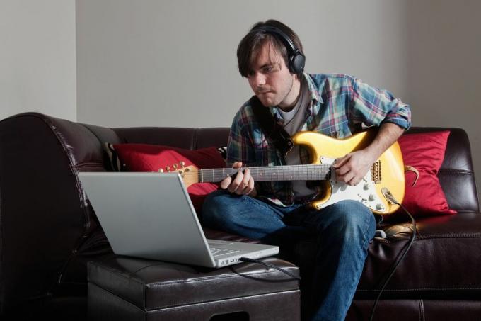 Uomo che suona la chitarra mentre guarda il laptop