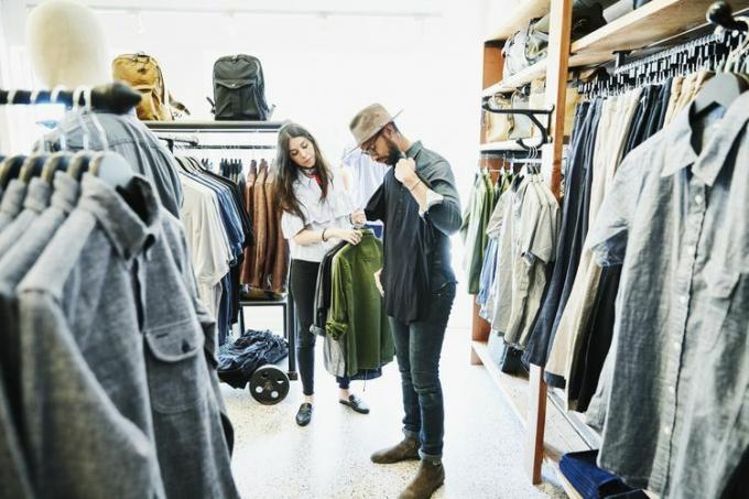 Магазинер помага на мъж да вземе решение за ризи, докато пазарува в бутик за мъжко облекло