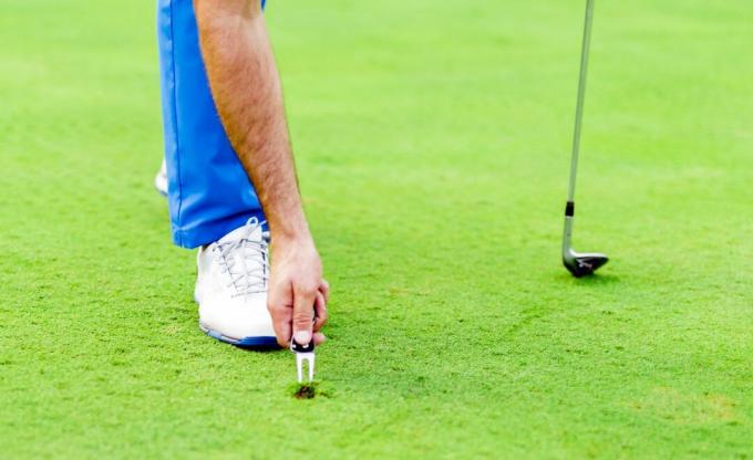 Golfo žaidėjas naudoja dvikovų taisymo įrankį golfo aikštelėje.