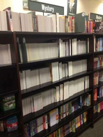 Knjižna polica z vsemi knjigami, obrnjenimi nazaj, tako da se hrbtenice ne vidijo. Nad polico je znak, ki pravi " Skrivnost".
