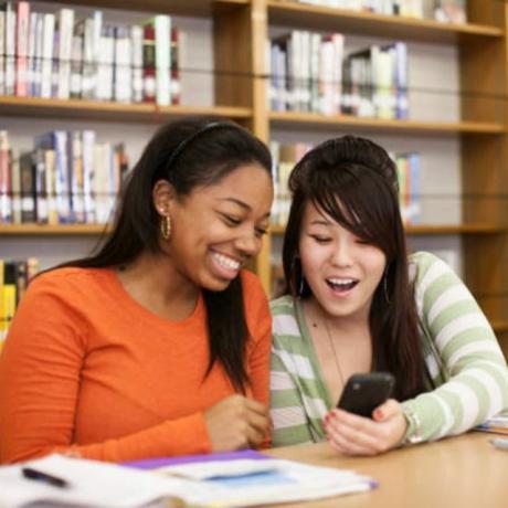 Nastoletnie dziewczyny patrzące na smartfon w bibliotece