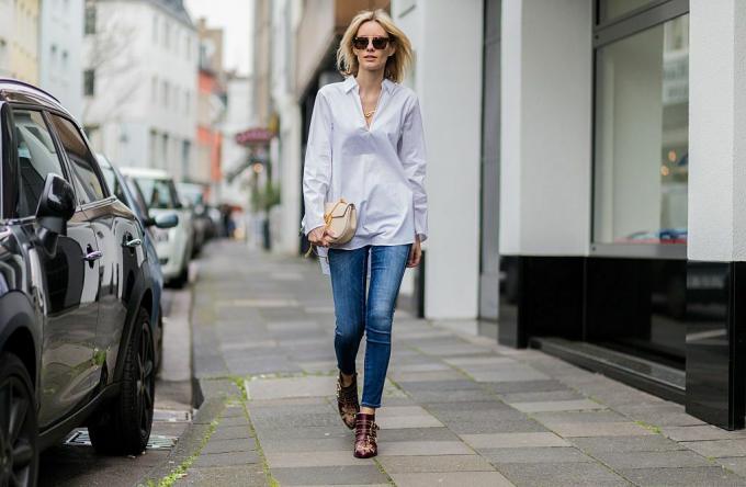 Supermodelo en jeans y camisa blanca caminando sobre una acera