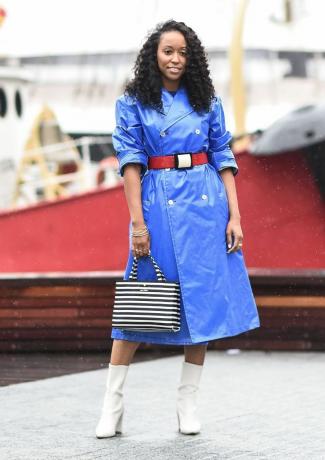 Frau in leuchtend blauem Regenmantel und gestreifter Handtasche und weißen Stiefeln
