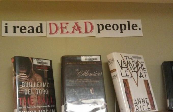 Bir kütüphane rafının fotoğrafı. Vampirleri içeren üç kitap rafta. Kitapların üzerinde " ÖLÜ insanları okuyorum" yazılı bir işaret var.