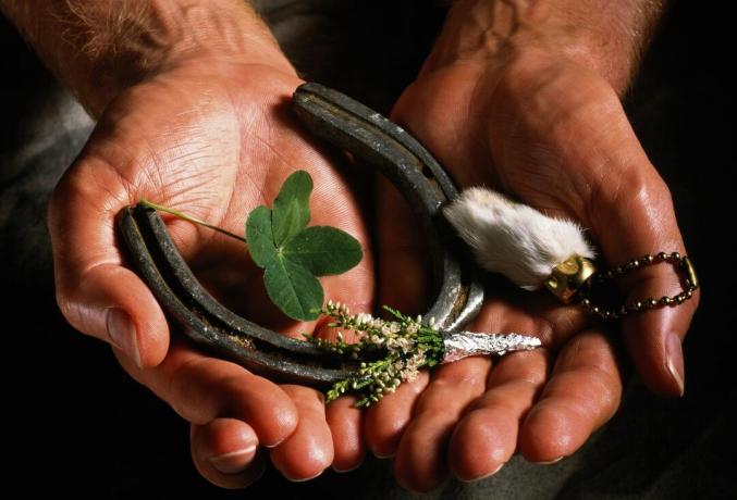 Mãos de homem segurando uma ferradura, trevo de quatro folhas e outros amuletos da sorte