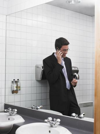 Мужчина разговаривает по мобильному телефону в ванной на рабочем месте.