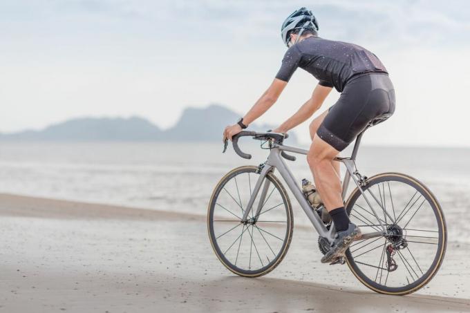 Genç Asyalı bisikletçi adam gün batımında sahilde bisiklete biniyor.