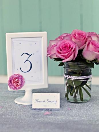 Eine Hochzeitstischkarte in einem Rahmen neben einer Vase mit Rosen.