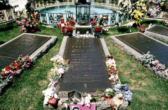 Mezar olarak kullanılan taş üzerinde dört uzun bronz panel, her mezarı çevreleyen çiçekler, demir çit, küçük yuvarlak havuz